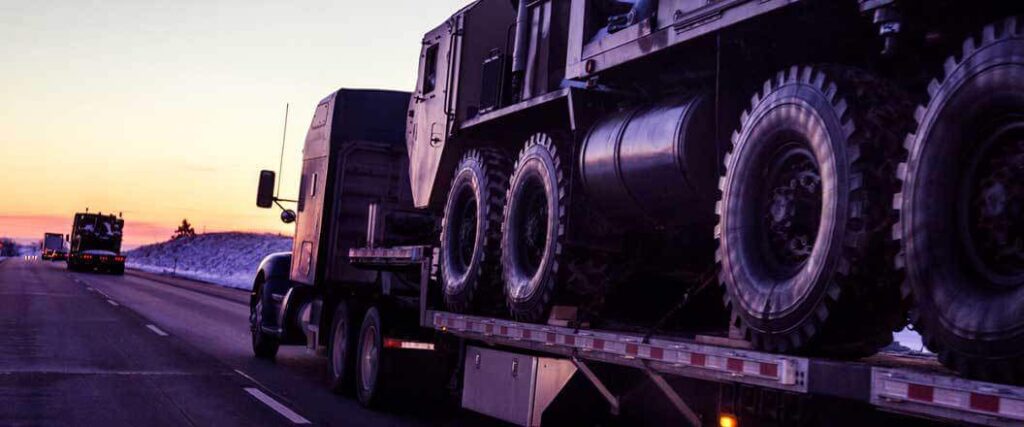 A semi truck transporting a military truck on the highway