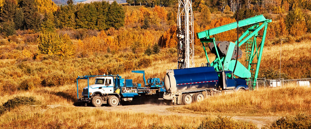 oilfield equipment hauling with a truck next to an oil rig in a field. 