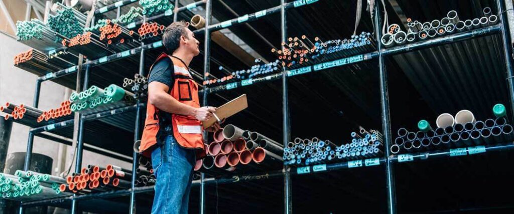 A warehouse worker performing inventory on several kinds of pipes.