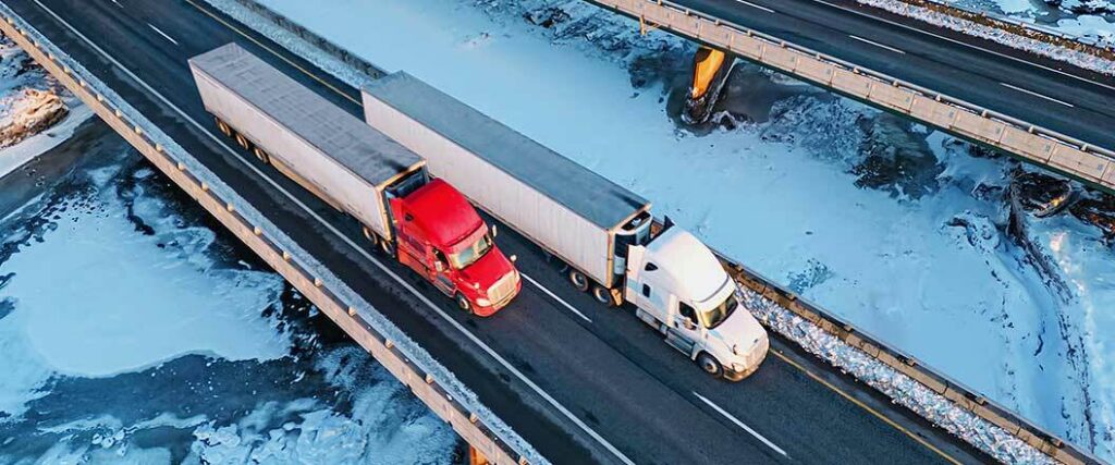 Two semi trucks traveling on an icy bridge. 